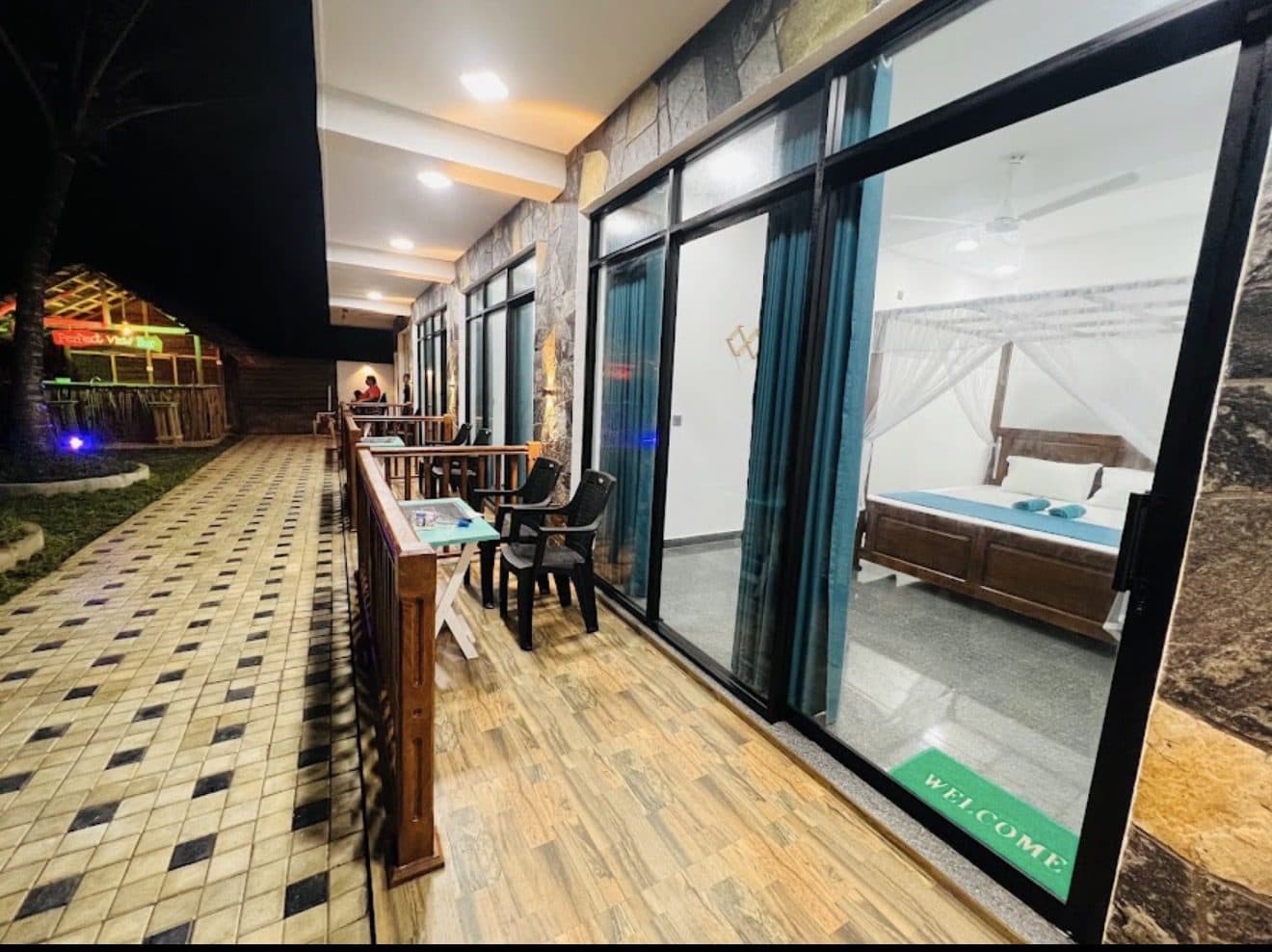 The walkway along the rooms at night, glass doors lit from inside